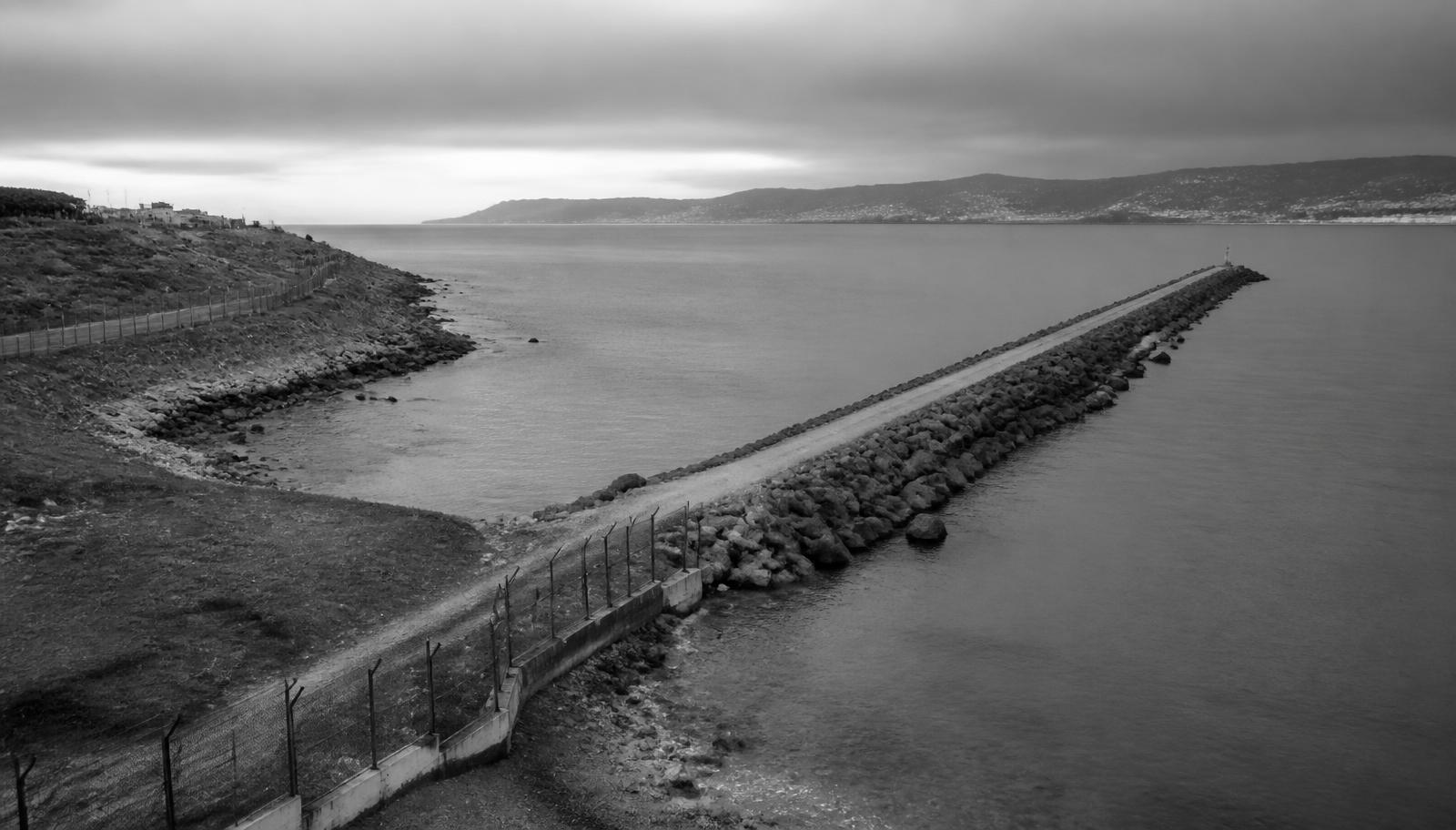 Espigón y línea costera fronteriza del Mediterráneo al amanecer, fotografía documental en blanco y negro sin presencia de personas